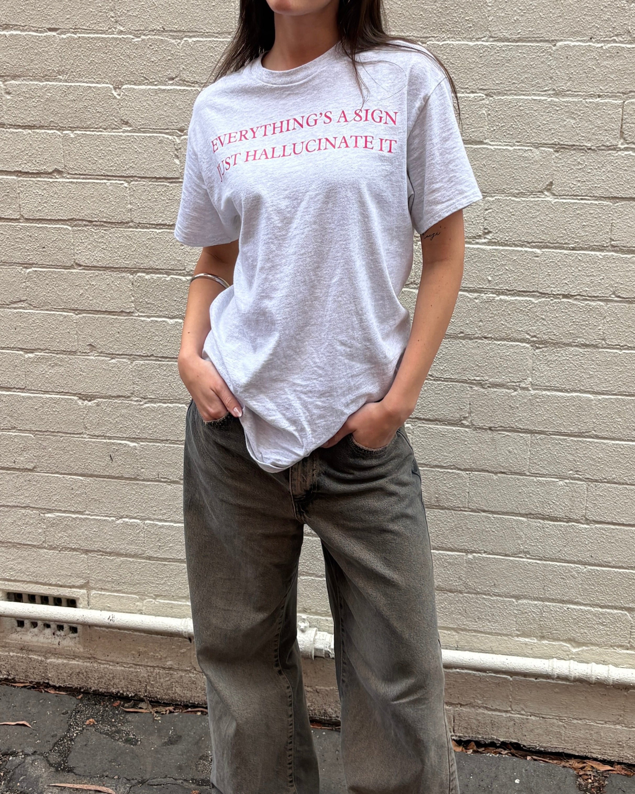 Person wearing a gray t-shirt with text standing against a brick wall.